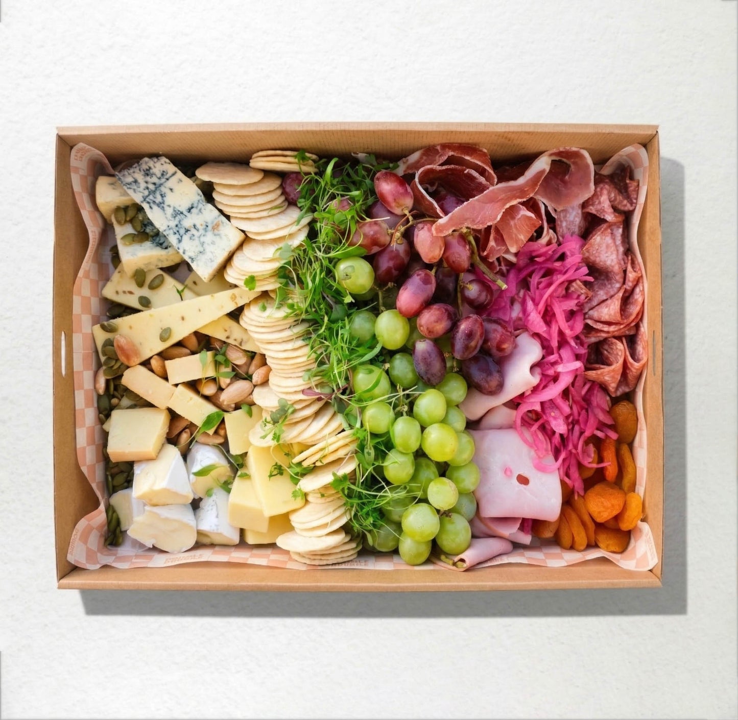 Assorted meats, cheeses, and fruits in a wooden box on a white background