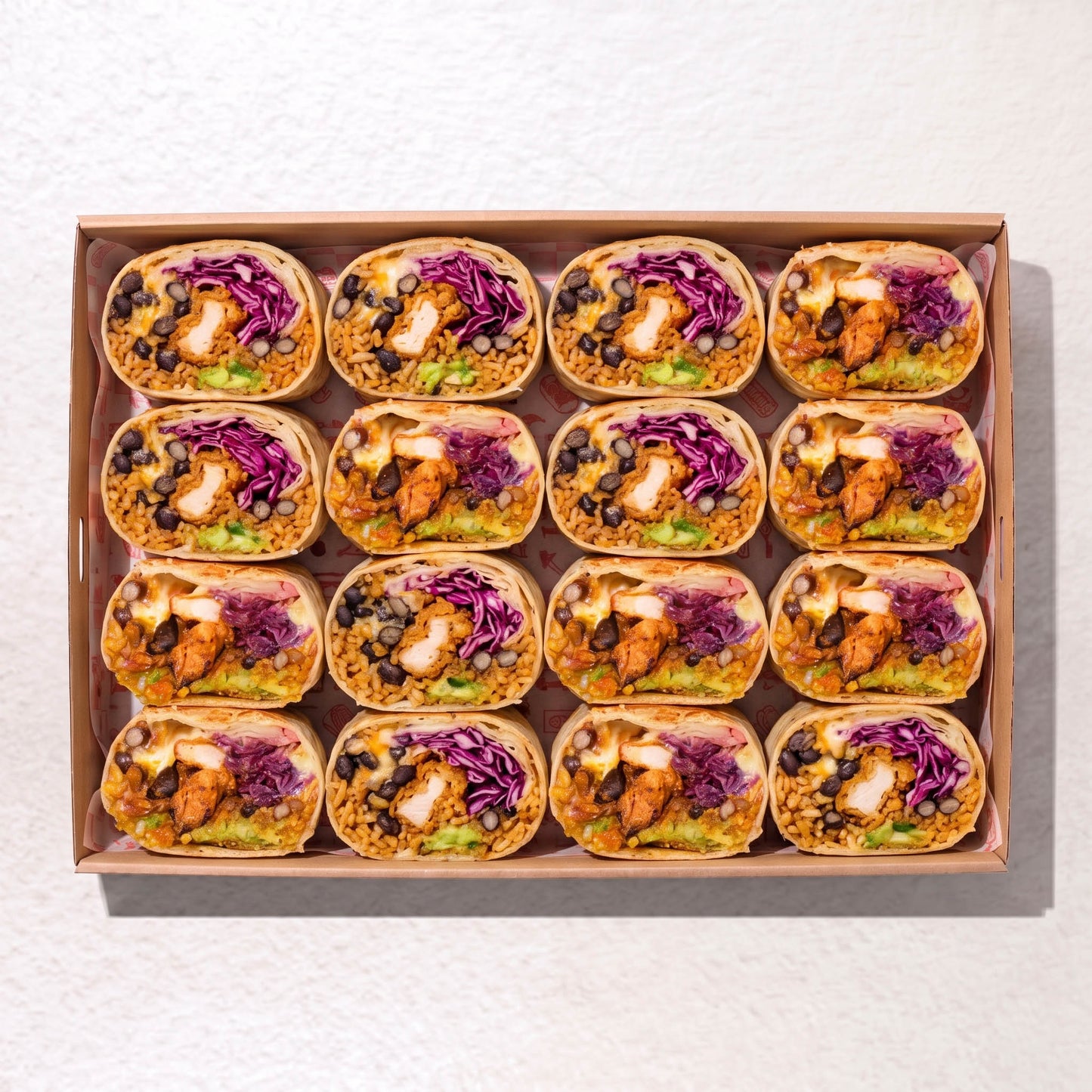 A top-down view of a brown cardboard tray holding 12 burritos arranged in a grid. Each burrito is filled with rice, black beans, avocado, shredded purple cabbage, and chicken. by Muy Muy Christchurch