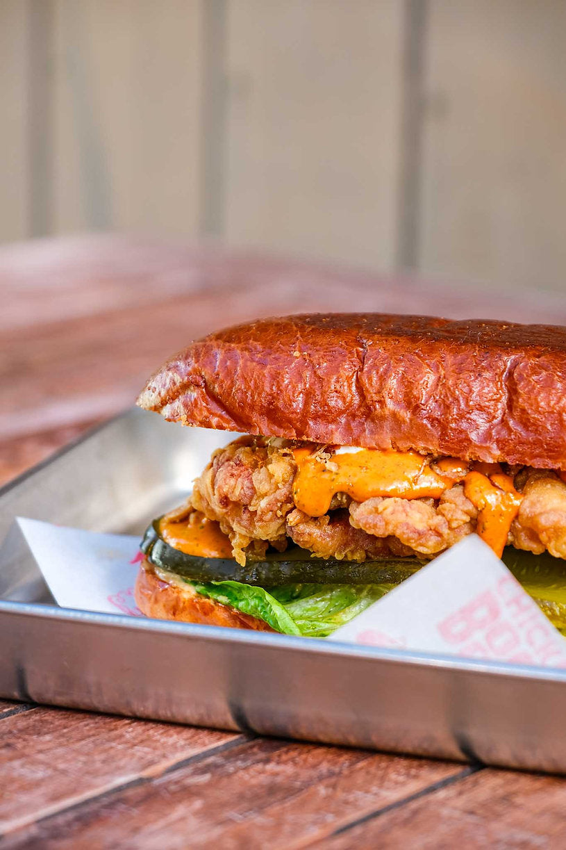 Burger with chicken patty, cheese, and lettuce on a metal tray with a wooden background