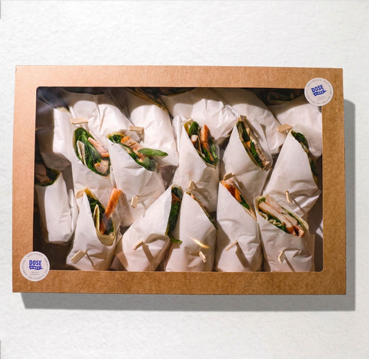 A square cardboard window box containing multiple wrapped food items, likely wraps or burritos, arranged inside on a white background. Two round stickers on the box read 'DOSE FOOD'.