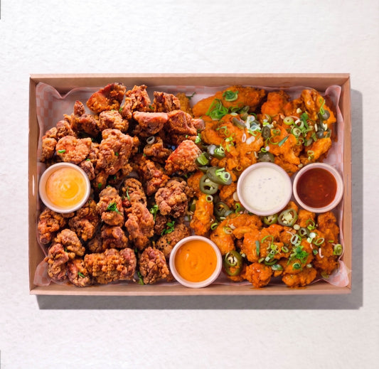 A top-down view of a cardboard food tray filled with two styles of fried chicken: crispy golden-brown fried pieces on the left and orange-battered pieces on the right with green onions, accompanied by four dipping sauces. by Boom Boom Chicken, in the Little High eatery, Christchurch 