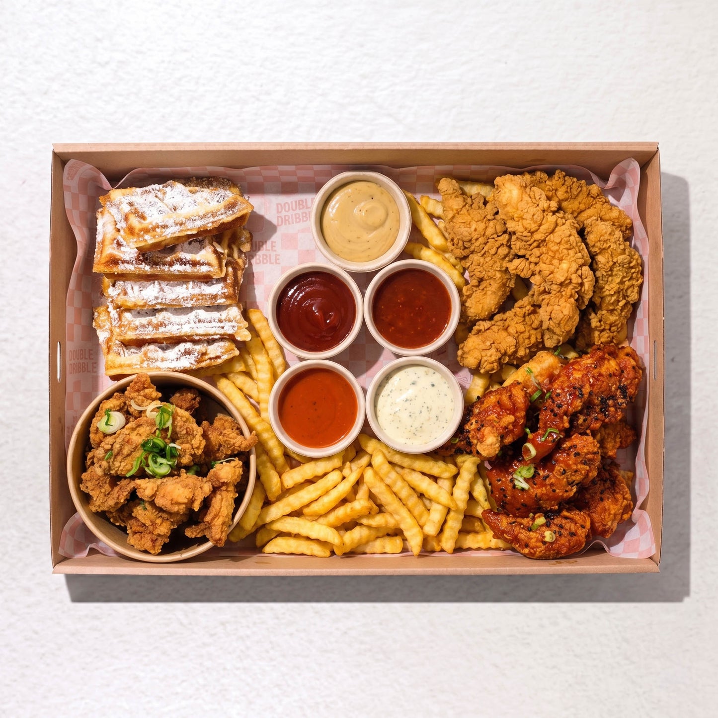 Tender Loving Platter from Double Dribble — golden crispy chicken tenders, sticky-glazed tenders, popcorn chicken and crinkle fries with house dipping sauces in a kraft catering box